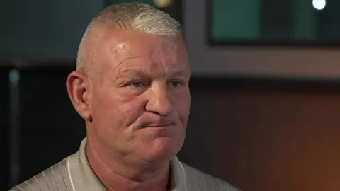 BBC A head and shoulders photo of Dean Windass during a BBC interview. He has short, grey hair and is wearing a silver shirt.