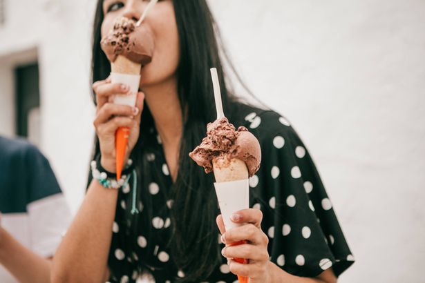 woman stands on street holding melting chocolate cone ice cream while looking at camera