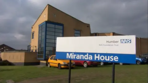 BBC The outside of Miranda House, Hull. The yellow brick building has blue window frames and stands behind a blue and white NHS sign.