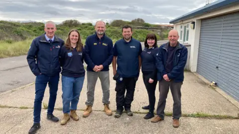 BBC / Simon Spark Four men and two women from the lifeboat crew at Spurn Point. They are standing outside the former station in RNLI dark blue branded clothing. 