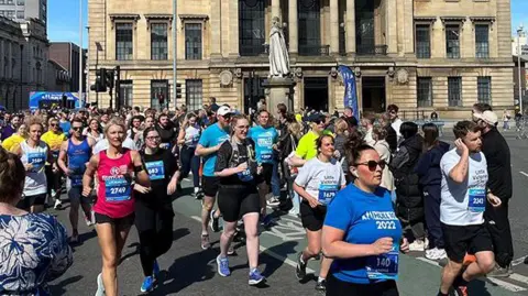 BBC Runners in last year's race passing Hull's Guildhall cheered on by spectators