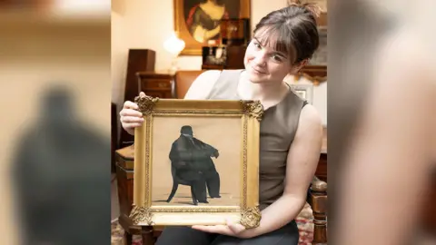 Duggleby Stephenson of York A portrait of a silhouette of the man once known as England's fattest is held by Holly Hammond from Duggleby Stephenson auction house. The painting is in a gold frame. 