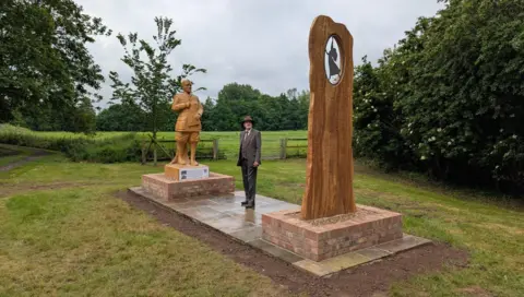 East Riding of Yorkshire Council Wooden sculpture of JRR Tolkien depicted in his army uniform and holding a notebook, along with a second sculpture depicting the writer's wife Edith danncing. There is a man standing between the two structures dressed in a suit and hat.