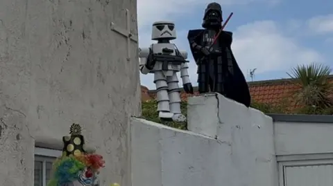 BBC/Amber Gash A white stormtrooper and a black Darth Vader stand on top of a white building.