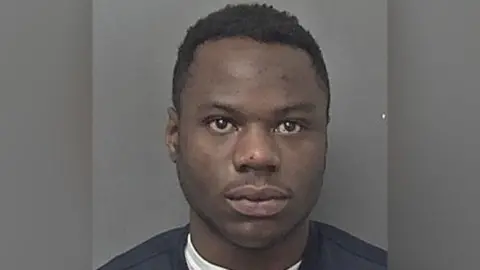 Humberside Police A man wearing a black jumper stands against a grey coloured wall and stares expressionless into the camera.