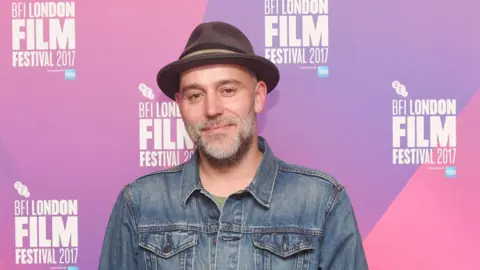 Getty Images / Rune Hellestad - Corbis A man in a hat and open neck shirt, smiles at the camera at a film awards ceremony