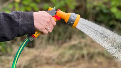 BBC Close up of a hand holding a hosepipe gun with a shower of water coming out of the nozzle