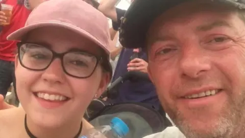 Scott Walker Bernadette Walker and Scott Walker are smiling at the camera in a selfie shot. She is wearing a pink baseball cap and he is also wearing a hat and has a stubbly beard