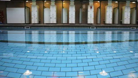 Getty Images An empty well-lit swimming pool, with changing rooms running along the poolside.