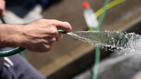 Getty Images A male hand holds the end of a hosepipe as water gushes out.