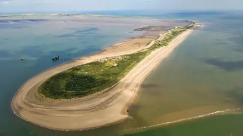 David Nichols Aerial view of a Spurn Point - a long piece of land with greenery in the middle and sand on the edges. The river water is surrounding it.