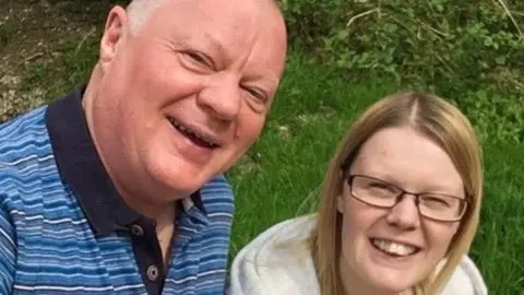 Leanne Fish A man in a striped shirt smiles next to his daughter, who wears a grey hoodie.