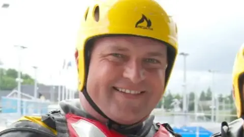 Family handout Man wearing a protective yellow helmet and life jacket. He is smiling.