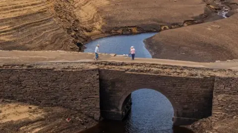 PA Media People walk over a bridge that is normally submerged by Baitings Reservoir in Ripponden.