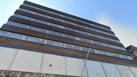 Google A towering concrete building with five rows of glass windows. The sky is blue.