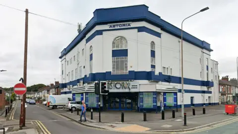 Google Exterior of the Astoria Bingo Club a large Art Deco former cinema which is painted white with dark blue strips along its roof and above the main door. It is located on a corner site on Holderness Road and Lake Drive 