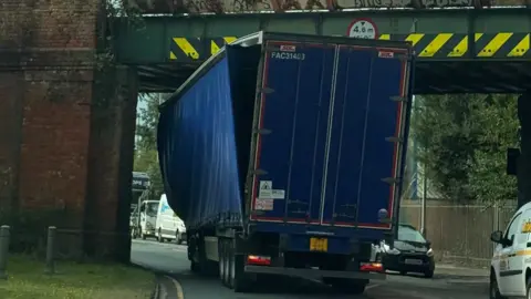 Isabella Norrison/BBC A lorry stuck under a railway bridge - there are yellow chevron markings at the top of the bridge - and the curtain on one side of the lorry is hanging off, with visible damage to the top of the vehicle.