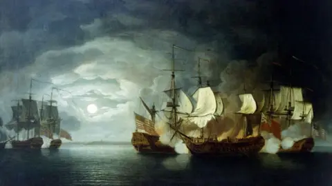Thomas Mitchell/Buyenlarge/Getty Images A painting of three 18th century ships firing towards a group of other ships who are gathered close by. They have white sails, the battle looks to be taking place at night with the moon visible in the background.