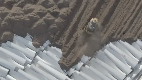 Getty A bulldozer is seen from drone footage piling soil on top of dozens of old wind turbine blades. 