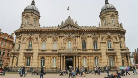 BBC View of the outside of the maritime museum, which is a two-storey Victorian building of yellow stone with two domes at the top. People are walking in front of it as they go about their daily business.