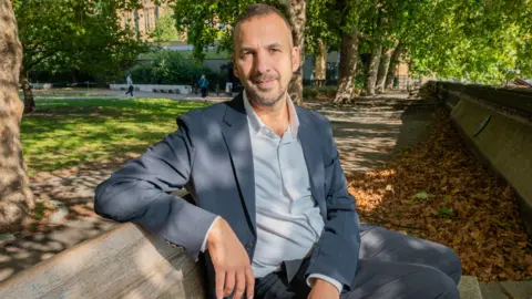 Getty Images The leader of the Green Party, Zack Polanski, sitting on a bench, with autumn leaves and trees in the background.