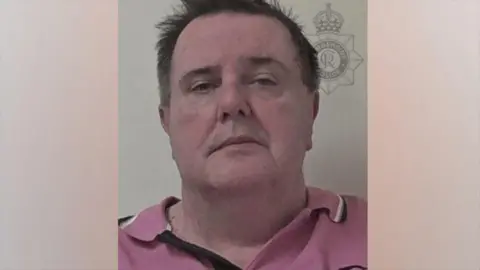 Humberside Police A police head and shoulders shot of a man with brown hair with some of the front sticking out. He is pulling a serious expression and wearing a pink polo shirt.
