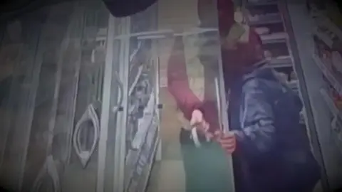 Old Town Store CCTV still of two shoplifters with hooded coats taking items from a fridge and loading them into a bag