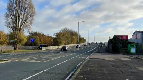 Hull City Council Hessle Road flyover with vehicles travelling away from the camera. Buildings are on the right. The sky is blue with clouds.