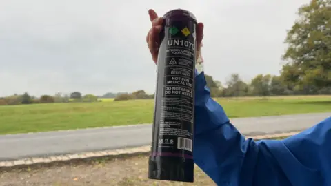 BBC/Jasmine Lowe One of the canisters found at Beverley Westwood, It is black and has multiple warning signs on the canister. The canister is about the size of the forearm of the lady who is holding it. 