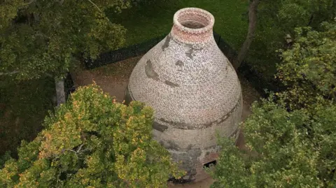 Historic England Drone view of conserved brickwork at the top of the kiln. The structure stands amid leafy trees and greenery.
