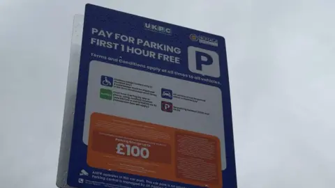 BBC News/ Jasmine Lowe A large red white and orange parking sign with lots of small print, but the fine amount in large bold writing