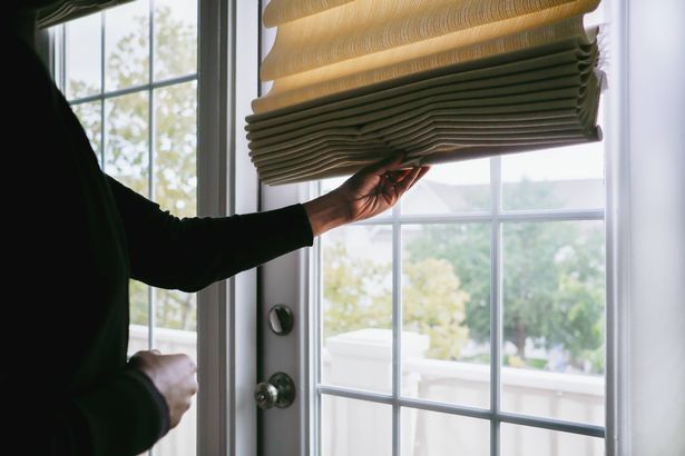 Close-up of unrecognizable black woman adjusting Roman shade on French door
