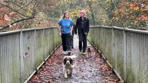 A group of women and two dogs walk across a bridge