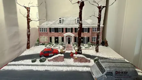 BBC/Gill Sennett The cake in the window it shows the two-storey red brick Home Alone house with icing snow on the roof and front lawns on the driveway is a confectionary car and van in the road