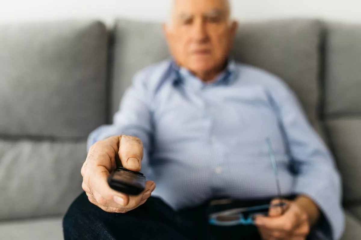 Senior man watching TV from the couch at home, focused on hand