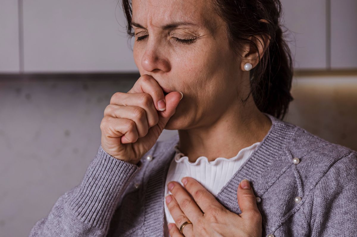 Woman covering her mouth while coughing in the kitchen.