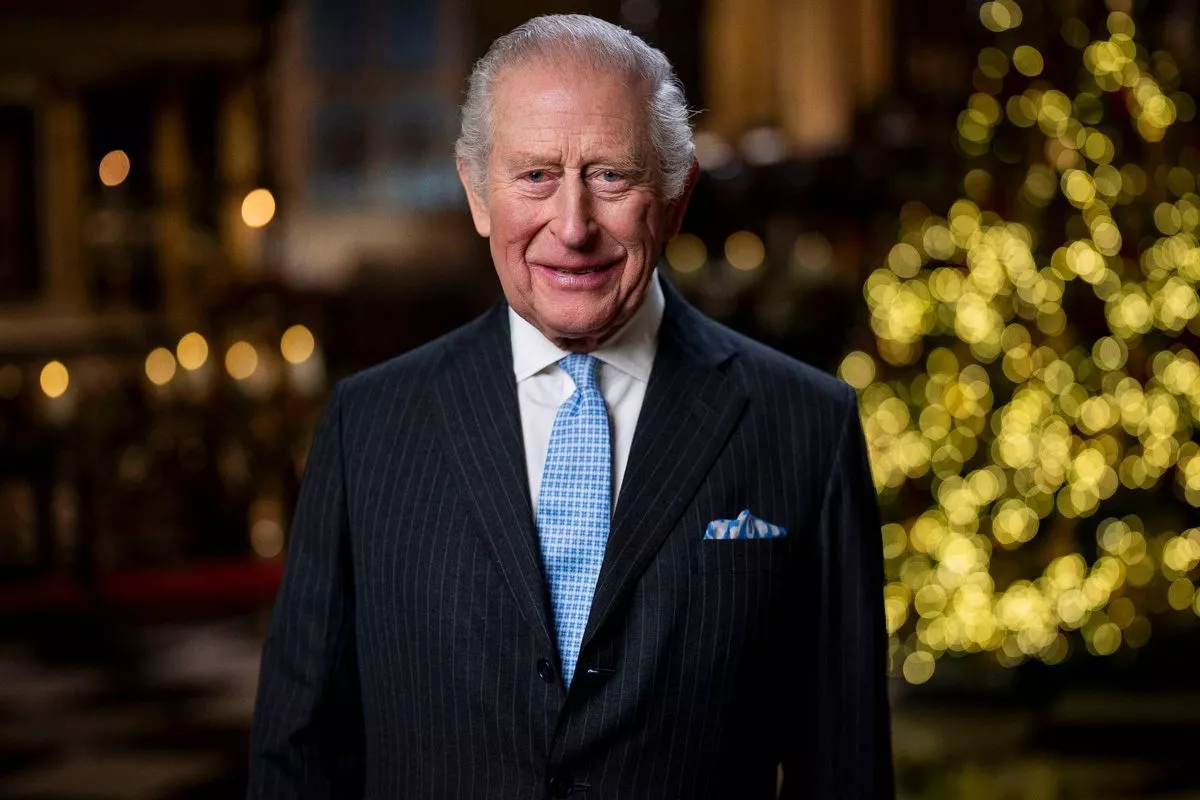 An individual dressed in a dark suit with a light blue tie stands in front of a glowing yellow background, smiling.