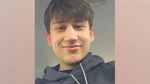 Kacper Bilengrek A portrait selfie of a young man wearing a black hoodie. He has brown hair with a fringe over his forehead and brown eyes. 