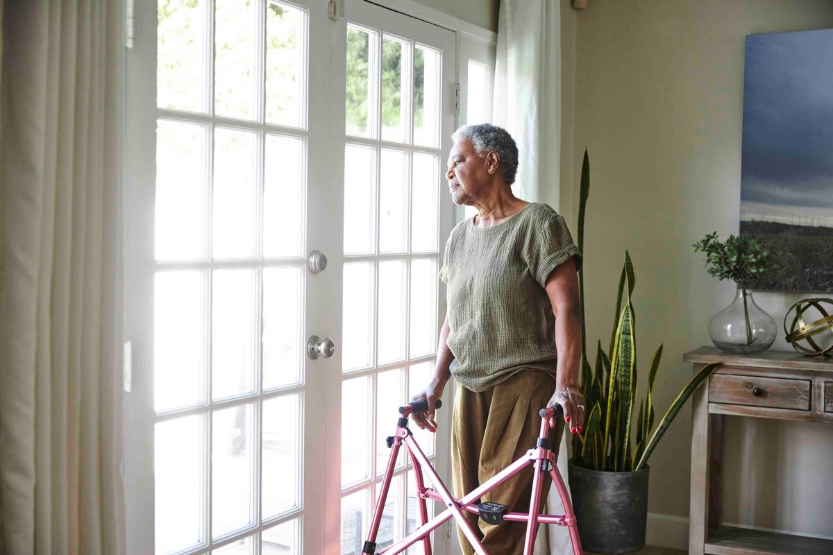 Senior woman looking through window while standing with walker at home