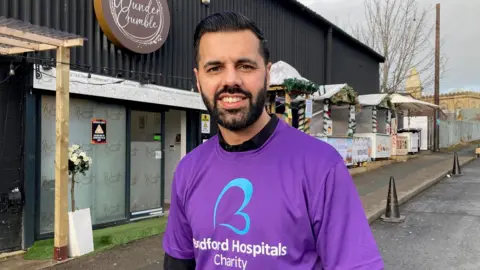 A bearded man wearing a purple T-shirt with white lettering on the front.