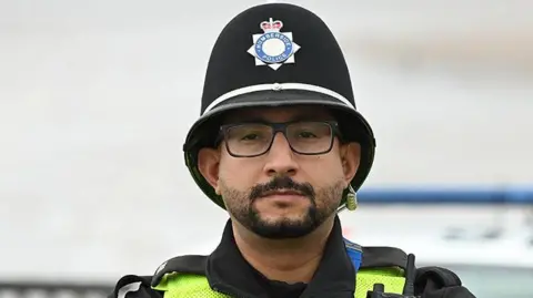 Police Federation PC Mourad Karaouani in his Humberside Police uniform with helmet, radio and body-worn camera. He has black hair and beard and wears glasses.