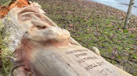 Jasmine Lowe/BBC A close up of the tree sculpture. It has the words "WHISPERING SWEET NOTHINGS HULL 2017 JB" carved in it.
