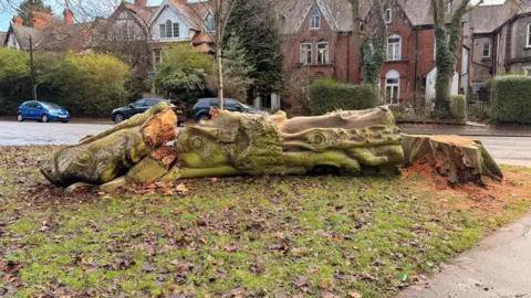 Hull City Council A decaying tree with a face carved into it is laid on its side after being chopped down. Residential houses can be seen in the background.