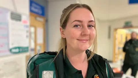 BBC Paramedic Rebecca Baldwin stands in a hospital corridor wearing her uniform.
