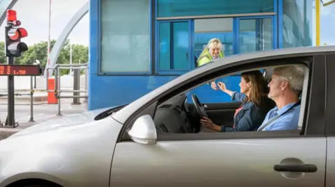 Getty Images A silver car containing a middle-aged man and woman, stopped at a toll booth. 