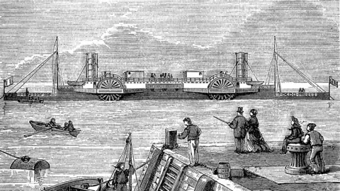 Duncan1890 / Getty Images Vintage black and white newspaper engraving of the SS Bessemer. It has four paddle wheels front and back and two funnels. It flies the French and British flags. A number of people stand on a quayside in the foreground watching it sail past.