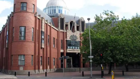 BBC The exterior of Hull Crown Court. It is a three-storey red brick building with a glass dome above its main entrance. There is a paved square at the front of the building with trees.