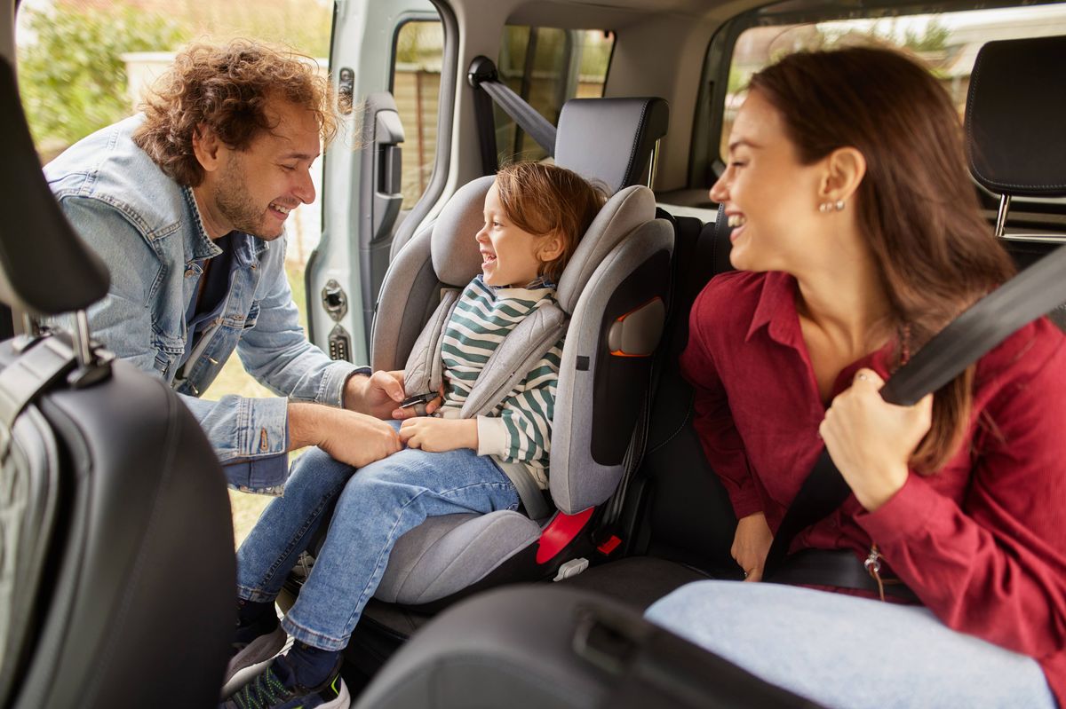 Father buckling son into car seat while mother sits beside, preparing for travel