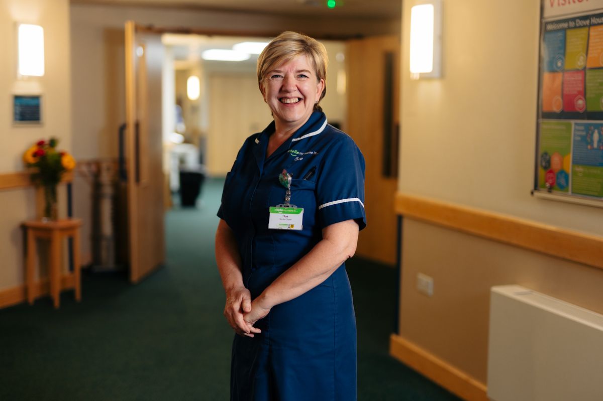Sue Fisher smiles at the camera in a corridor of Dove House Hospice while wearing her nurse's uniform