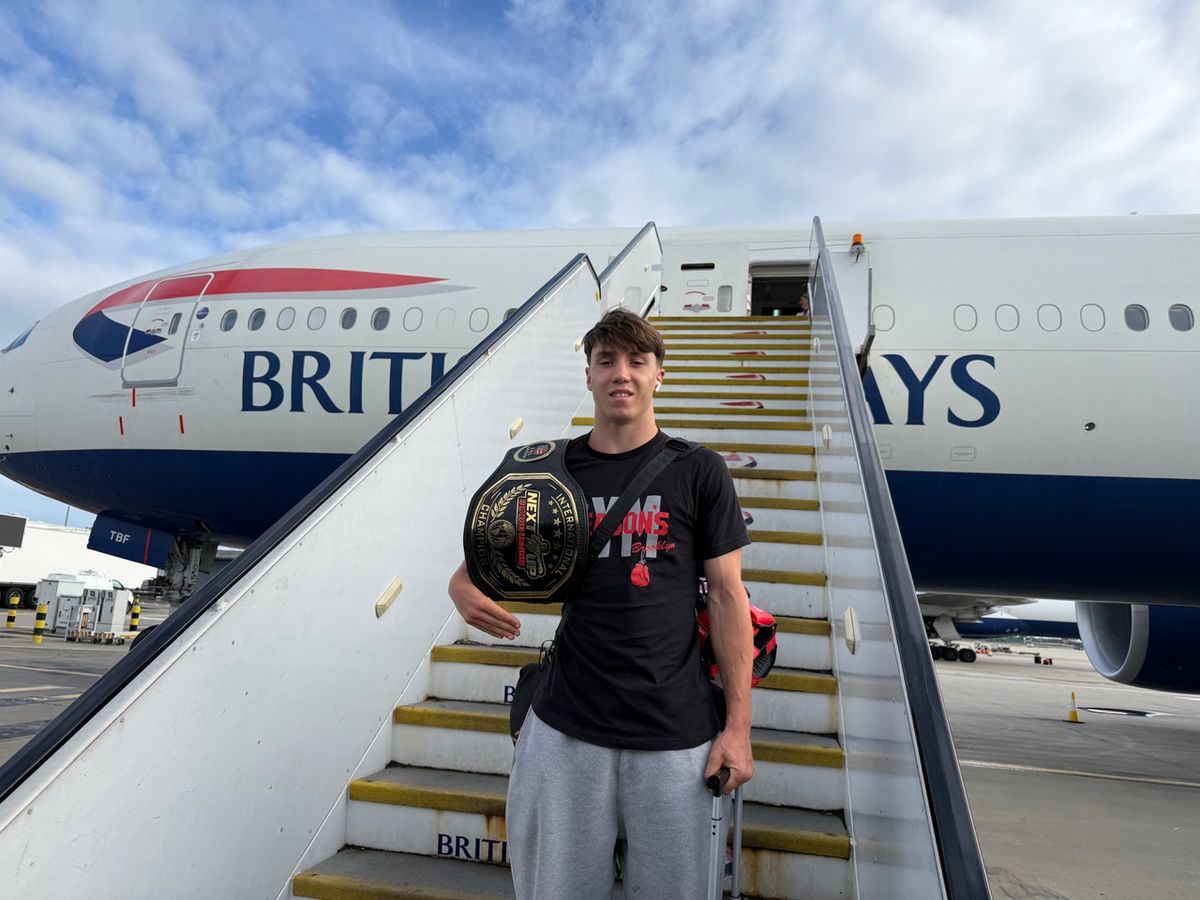 Saul Matchett at the end of the British Airways airplane steps with his winning belt and his suitcase